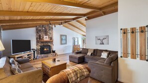Ein gemütliches Wohnzimmer mit Kamin aus Stein, Holzbalken, einem Fernseher und einer Couch.