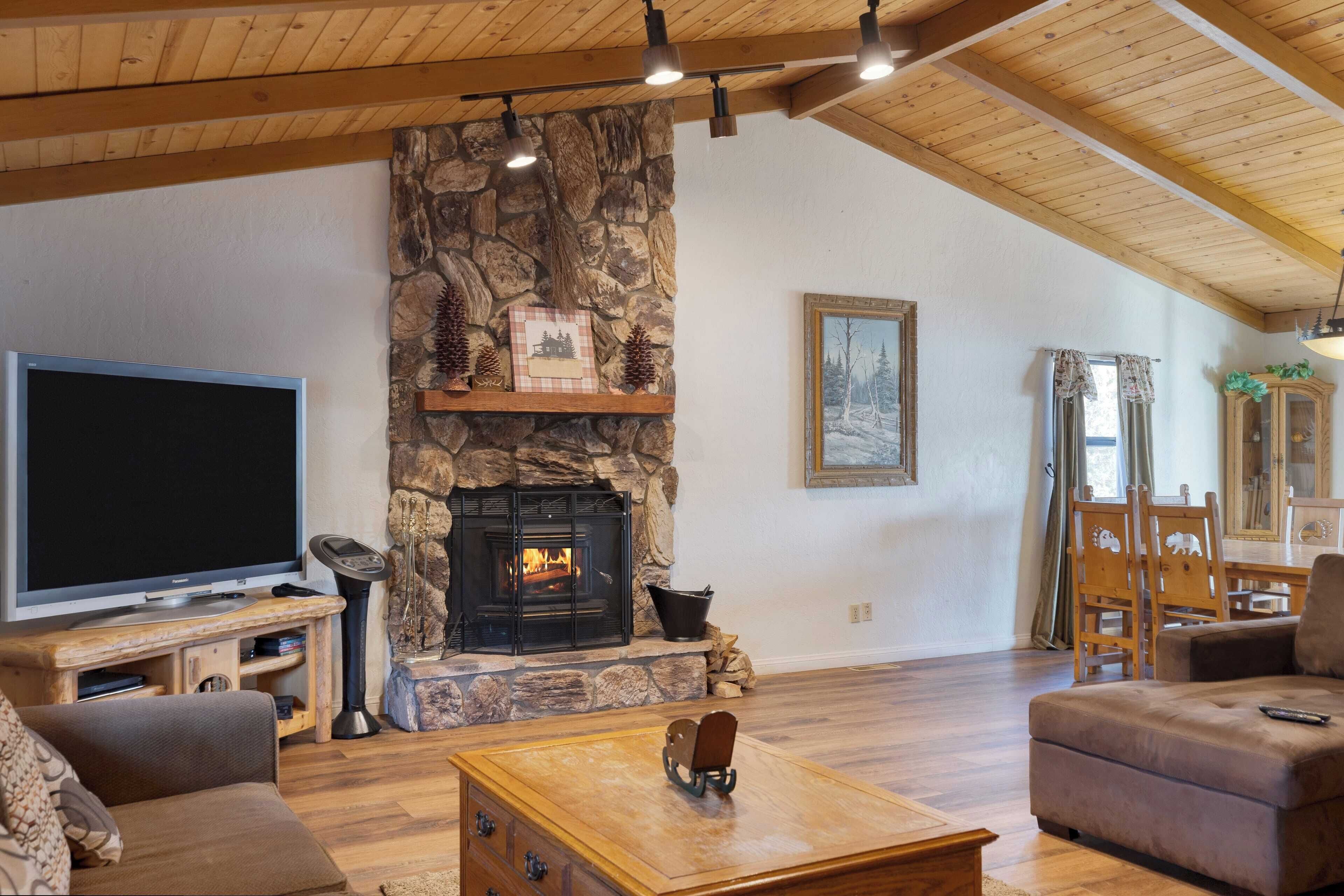 Una sala de estar acogedora con chimenea de piedra, vigas de madera en el techo, televisor de pantalla plana y asientos cómodos.
