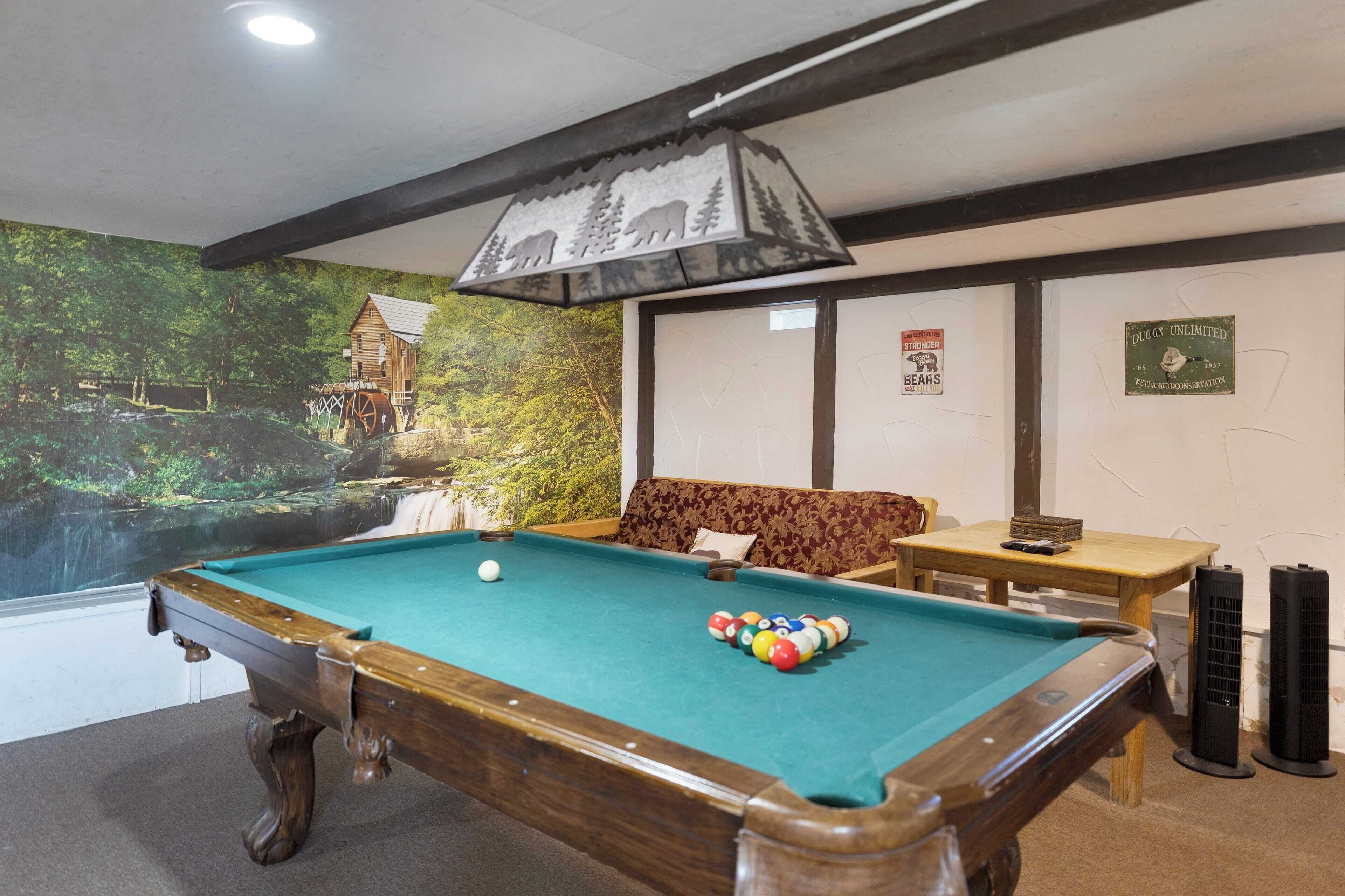 A pool table with a green felt surface, surrounded by a wooden frame. There is a sofa and a small table with a box on it.