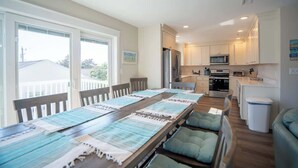 Ruime eethoek met een lange tafel, comfortabele stoelen en uitzicht op de keuken en het buitenbalkon.