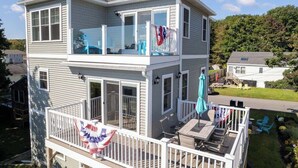 Een huis met twee verdiepingen, een balkon en een terras met tuinmeubilair, en een vlag.