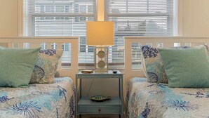 A room with two beds, each with floral-patterned bedding and matching pillows. A bedside table with a lamp and a decorative item is between the beds.