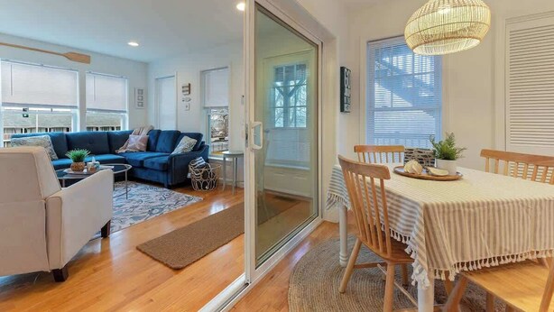 A modern living room with a blue sofa, a white armchair, and a dining area with a table and chairs.