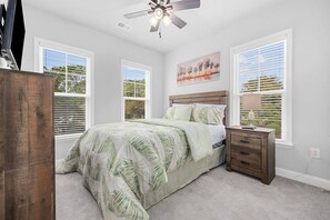 Ein Schlafzimmer mit einem Bett, einem Nachttisch, einem Deckenventilator und Fenstern mit Jalousien.