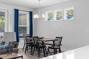 Ein moderner Essbereich mit einem Holztisch, schwarzen Stühlen, einer Chandelüster und Blick auf Bäume durch die Fenster.