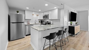 Una cocina moderna con una isla central, electrodomésticos de acero inoxidable y taburetes negros.