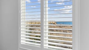 Una ventana con persianas blancas, con vista a una playa y una estructura de madera.