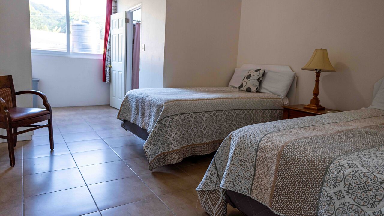 A room with two beds, a chair, a lamp, and a window with curtains.