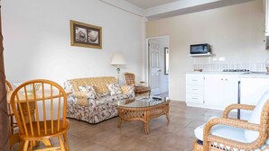 Ein Wohnzimmer mit einer Couch, Sesseln, einem Couchtisch, einer Lampe und einer Küchenzeile mit einer Mikrowelle.