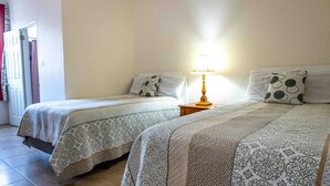 Ein Hotelzimmer mit zwei Betten, jeweils mit gemusterten Bettbezügen und Kissen, einem Nachttisch mit Lampe und einer Tür mit Vorhang.