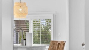 Eine moderne Küche mit weißen Schränken, einer Essgelegenheit aus Holz und einem großen Fenster mit Jalousien.