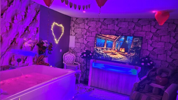 A room with a stone wall, a large flat-screen TV, a massage chair, and a bathtub. - Spa Suite la caverne Private terrace (Montpellier)