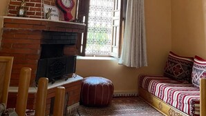 A cozy room with a brick fireplace, a wooden bench, and a patterned bed. - Gite Mrbie (Oum Rabia)