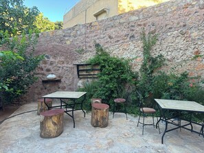 An outdoor patio with stone flooring, rustic wooden stools, metal tables, and chairs.