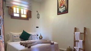 A neatly arranged bedroom with a bed, pillows, a decorative lamp, a wooden ladder, and a patterned rug. - Gite Mrbie (Oum Rabia)