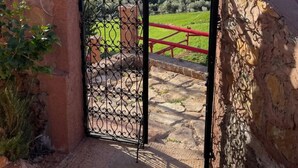 A wrought iron gate leading to a stone wall with a red railing, overlooking a hilly landscape. - Gite Mrbie (Oum Rabia)