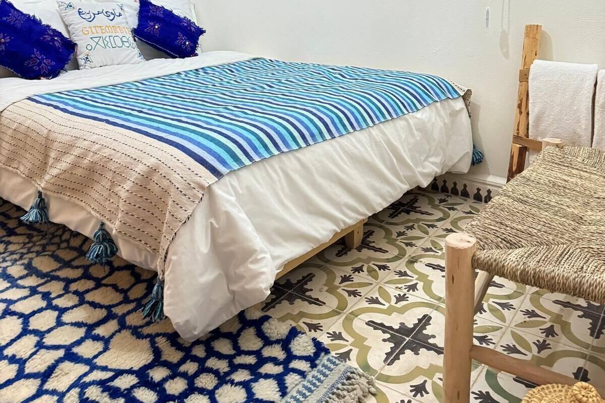 A bedroom with a bed, a wooden wardrobe, a hanging light fixture, and a patterned rug.