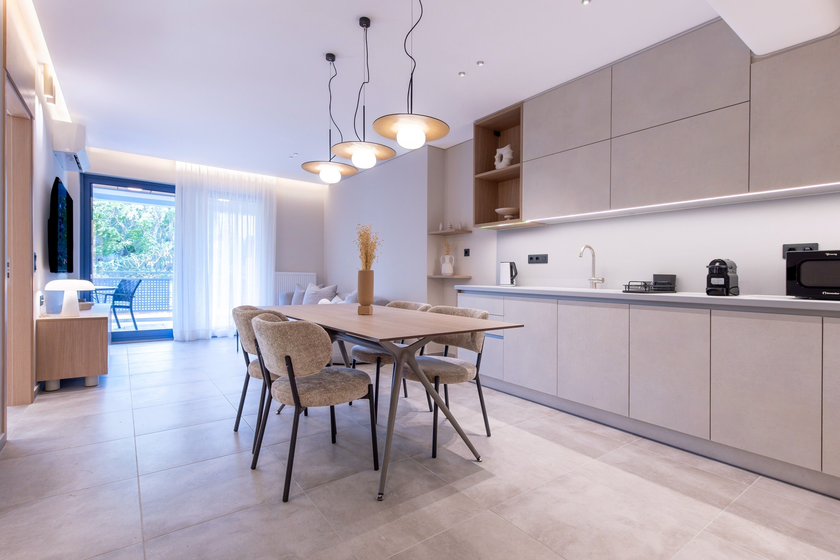 A modern kitchen with a dining area, featuring a wooden table and chairs, pendant lights, and built-in cabinets.
