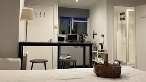 Ein Hotelzimmer mit einem Bett, einem kleinen Schreibtisch, einem Stuhl, einer Lampe, einer Dusche und einer Küchenzeile.
