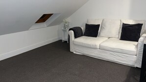 Ein weißes Ledersofa mit schwarzen Kissen in einem Raum mit schrägverdeckter Decke und einem kleinen weißen Tisch mit einem Blumenstrauß.