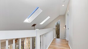 A spacious hallway with wooden flooring, white railings, and skylights.