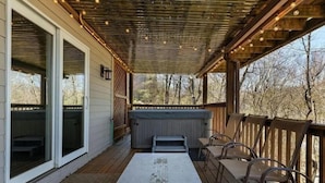 A covered deck with a hot tub, outdoor seating, and a view of trees.