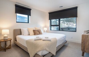 Un dormitorio moderno con una cama grande, dos lámparas de noche, una mesita de madera y vistas a un paisaje nevado por las ventanas.
