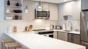 Eine moderne Küche mit weißen Schränken, einem Edelstahlkühlschrank, einer Mikrowelle und einer großen Kochinsel mit Sitzgelegenheiten.