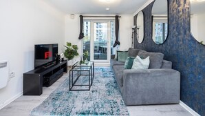 A modern living room with a grey sofa, black entertainment unit, and a large mirror.