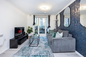 A modern living room with a grey sofa, black entertainment unit, and a large mirror.