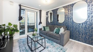 A modern living room with a grey sofa, a glass door leading to a balcony, and a blue textured wall.