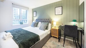 A bedroom with a bed, bedside table, chair, and a window with blinds.