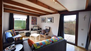 A modern living room with a sofa, armchair, and coffee table. There is a TV, a small table, and a window with curtains. - Holiday Home in De Haan With Garden (De Haan)