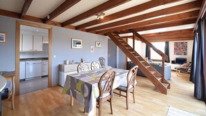 A spacious living area with a wooden staircase, a dining table with chairs, and a kitchen area with cabinets and a dishwasher. - Holiday Home in De Haan With Garden (De Haan)