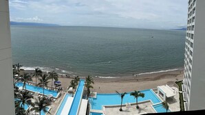 Vista de una playa con zona de piscina, palmeras y un edificio en primer plano.
