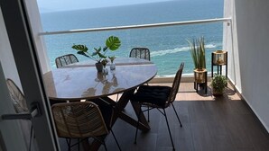 Un balcón con mesa y sillas, vista al océano y plantas en macetas.