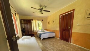 Ein Hotelzimmer mit zwei Betten, einem Deckenventilator, einer Tür und einem Vorhangfenster.