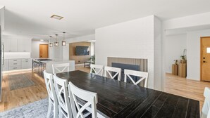 A modern kitchen with white cabinets, a central island, and a dining area with a dark wooden table and white chairs. - Charming 4 bedroom, 3 bathroom Brick Home located on 3 rural acres. (Colton)