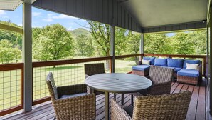 A covered outdoor deck with wicker furniture, a round table, and a view of a green landscape.