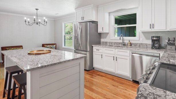 A modern kitchen with white cabinets, a stainless steel refrigerator, a built-in dishwasher, and a granite countertop.