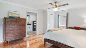 A bedroom with a wooden bed, a dresser, a ceiling fan, and a view of a bathroom through an open door.