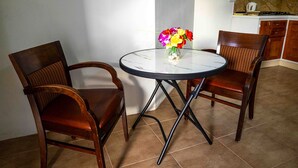 Un comedor con dos sillas de madera y una mesa redonda, un jarrón con flores y una cocina al fondo.