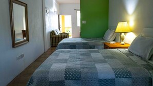 Habitación de hotel con dos camas, una pared de acento verde, una mesita de noche con lámpara y vistas al balcón exterior.