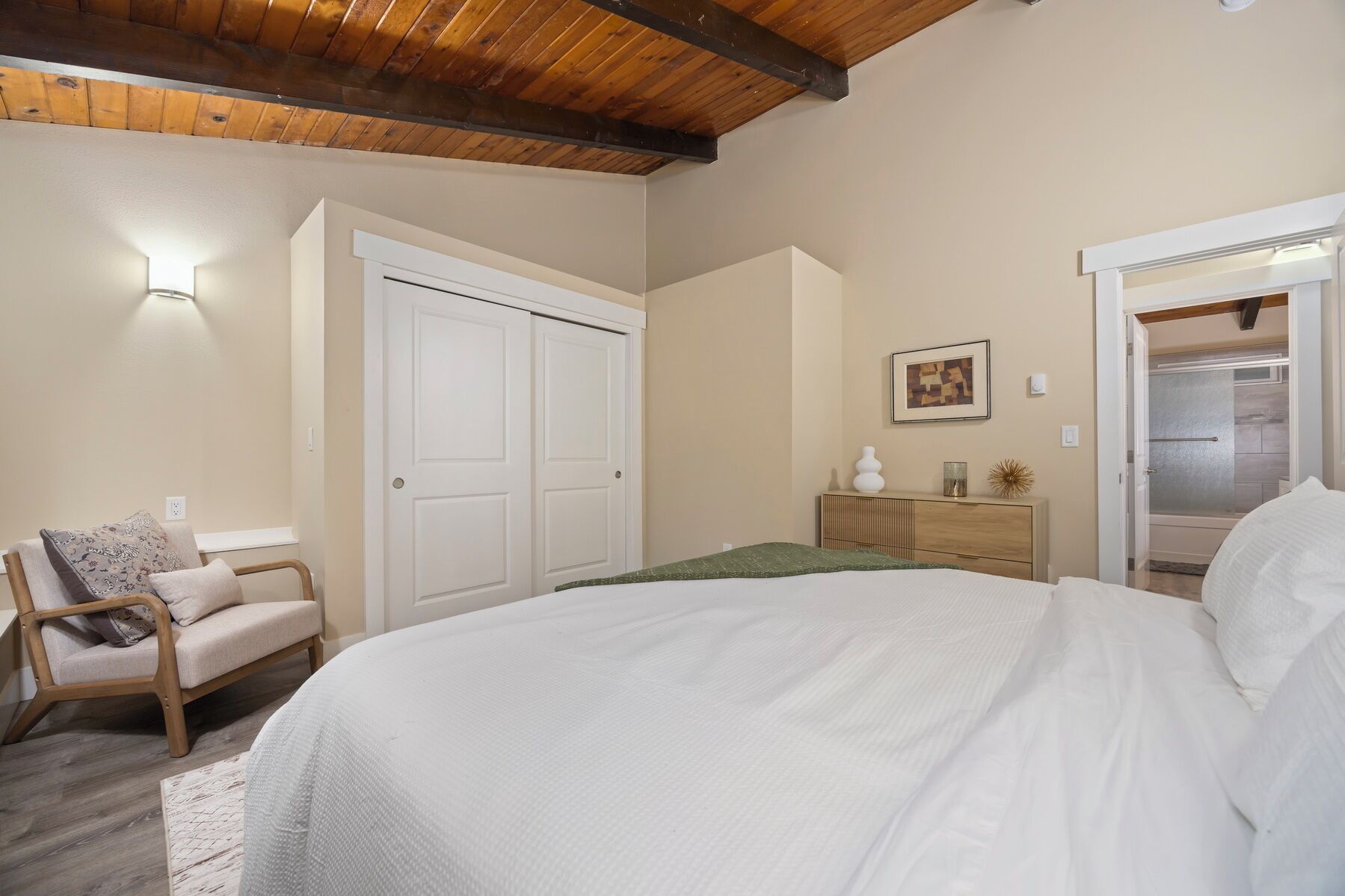 A bedroom with a large bed, a wooden ceiling, a wardrobe, a dresser, and a chair.