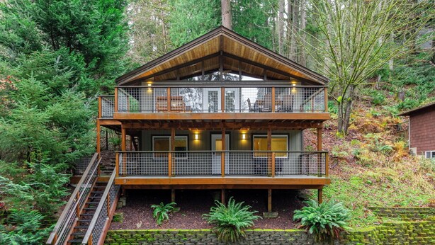 Une cabane en bois à deux étages, dotée d’un balcon et entourée d’une forêt dense.