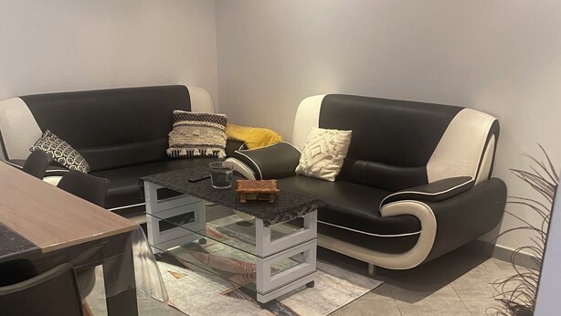 Una sala moderna con un juego de sofá blanco y negro, una mesa de centro de vidrio y una pequeña mesita de madera.