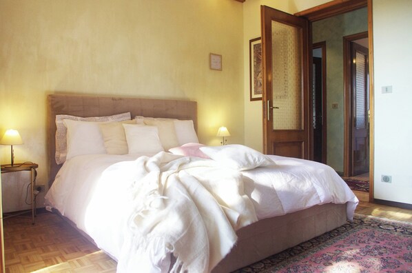 Een slaapkamer met een groot bed, twee bedlampen, een houten hoofdbord en een deur naar een andere kamer.