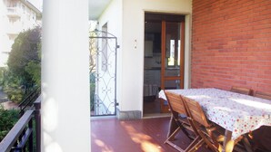 Un balcón con una mesa y sillas, vistas de un edificio y una puerta que da a un espacio interior.