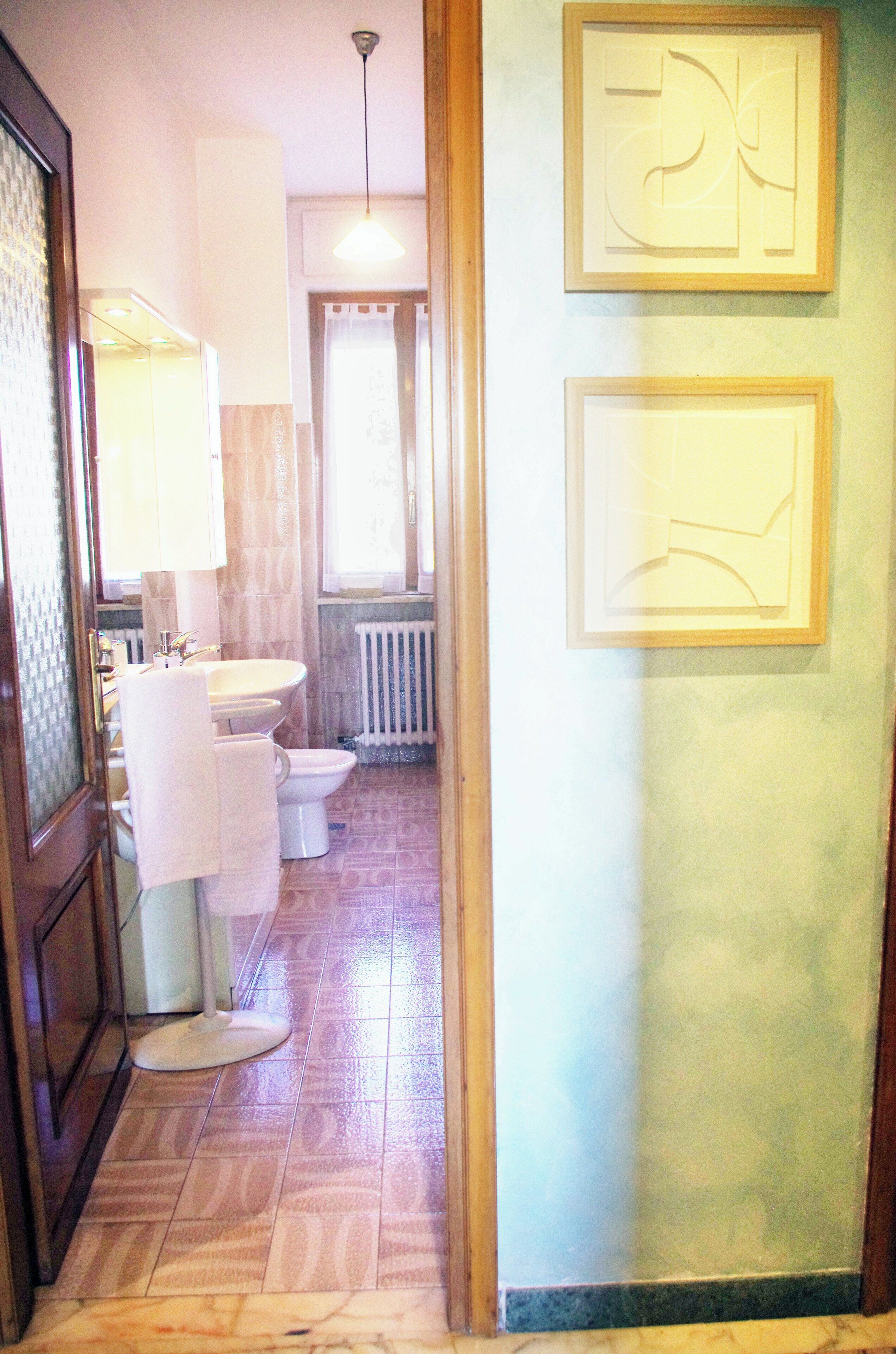 A bathroom with a toilet, sink, and mirror. There are framed pictures on the wall and a towel hanging on the door.