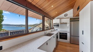 Una cocina moderna con un amplio ventanal que ofrece vistas panorámicas, electrodomésticos integrados y techo de madera.